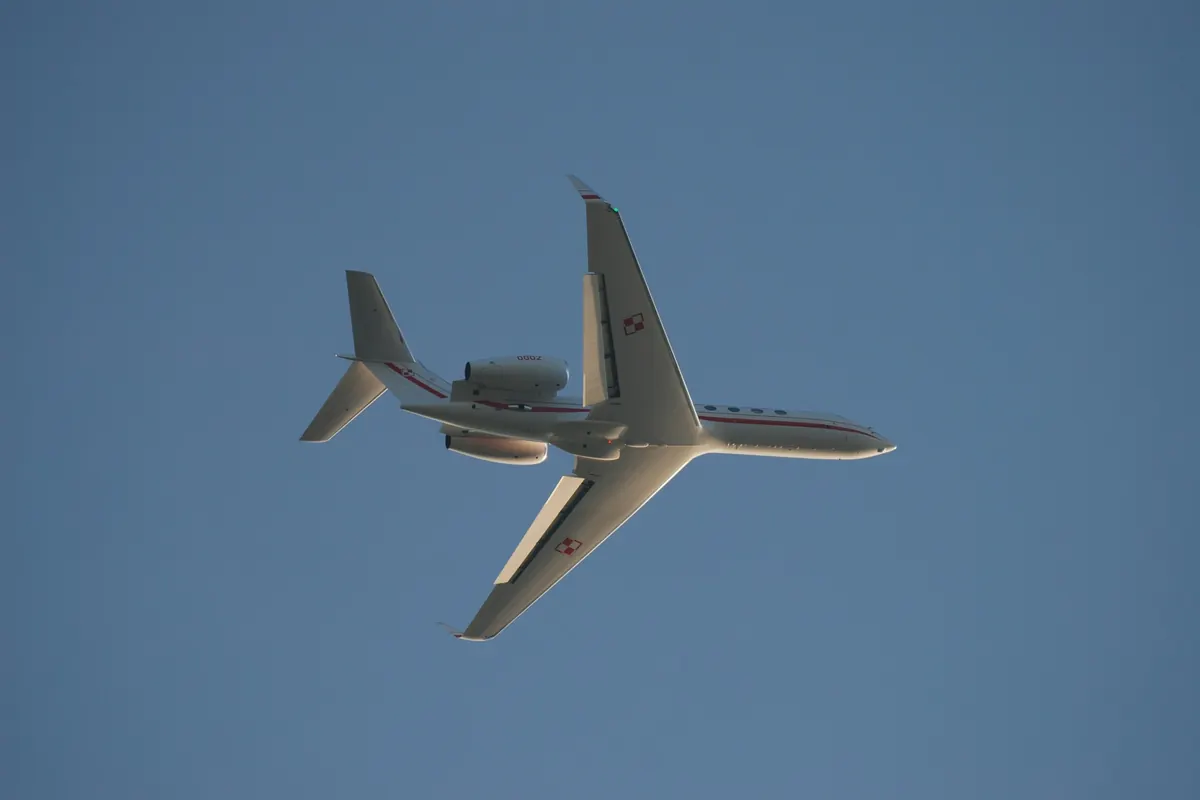 Underside of a business jet in flight against a pale sky